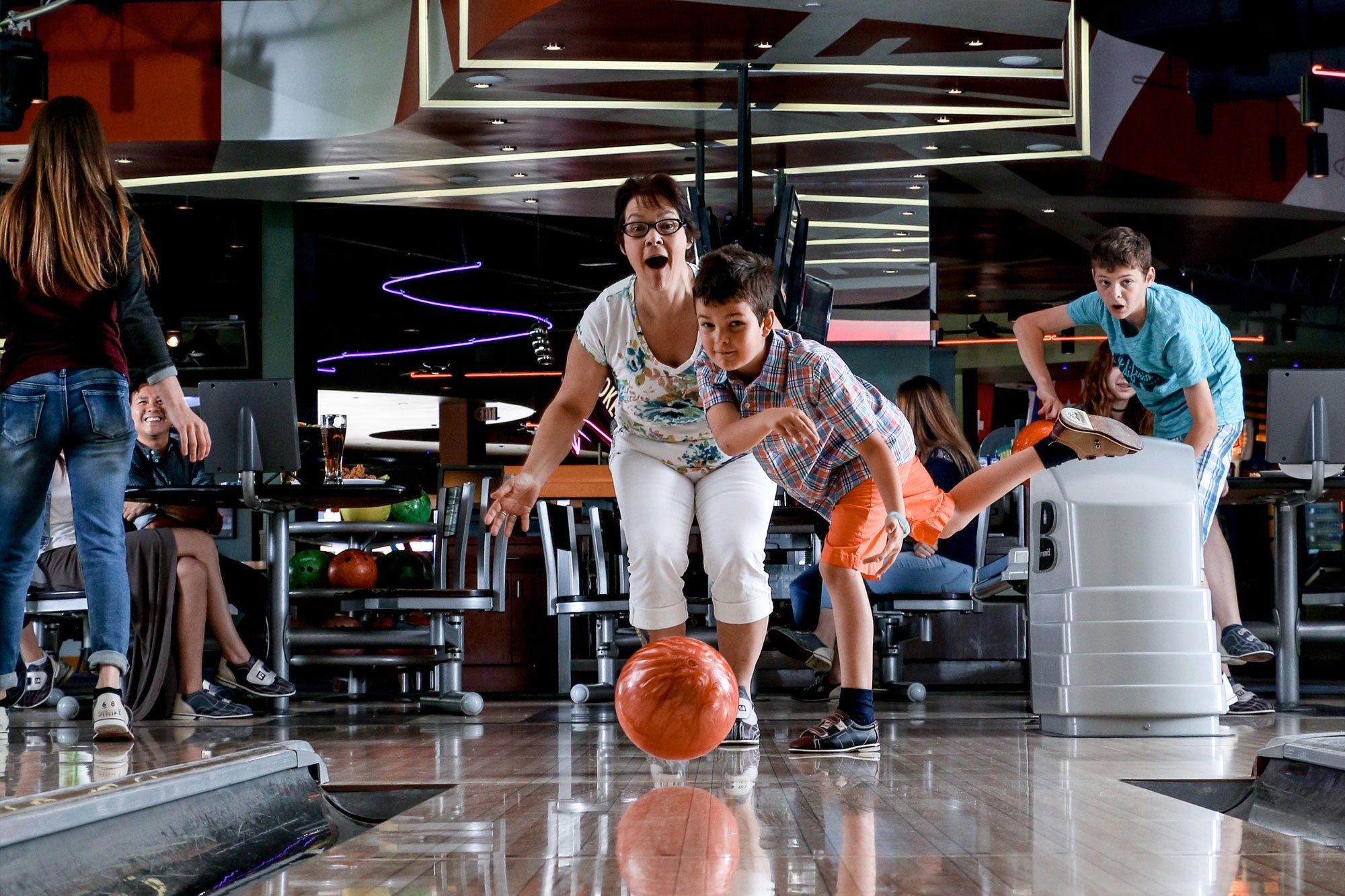 Mom bowling with son watching ball go down lane
