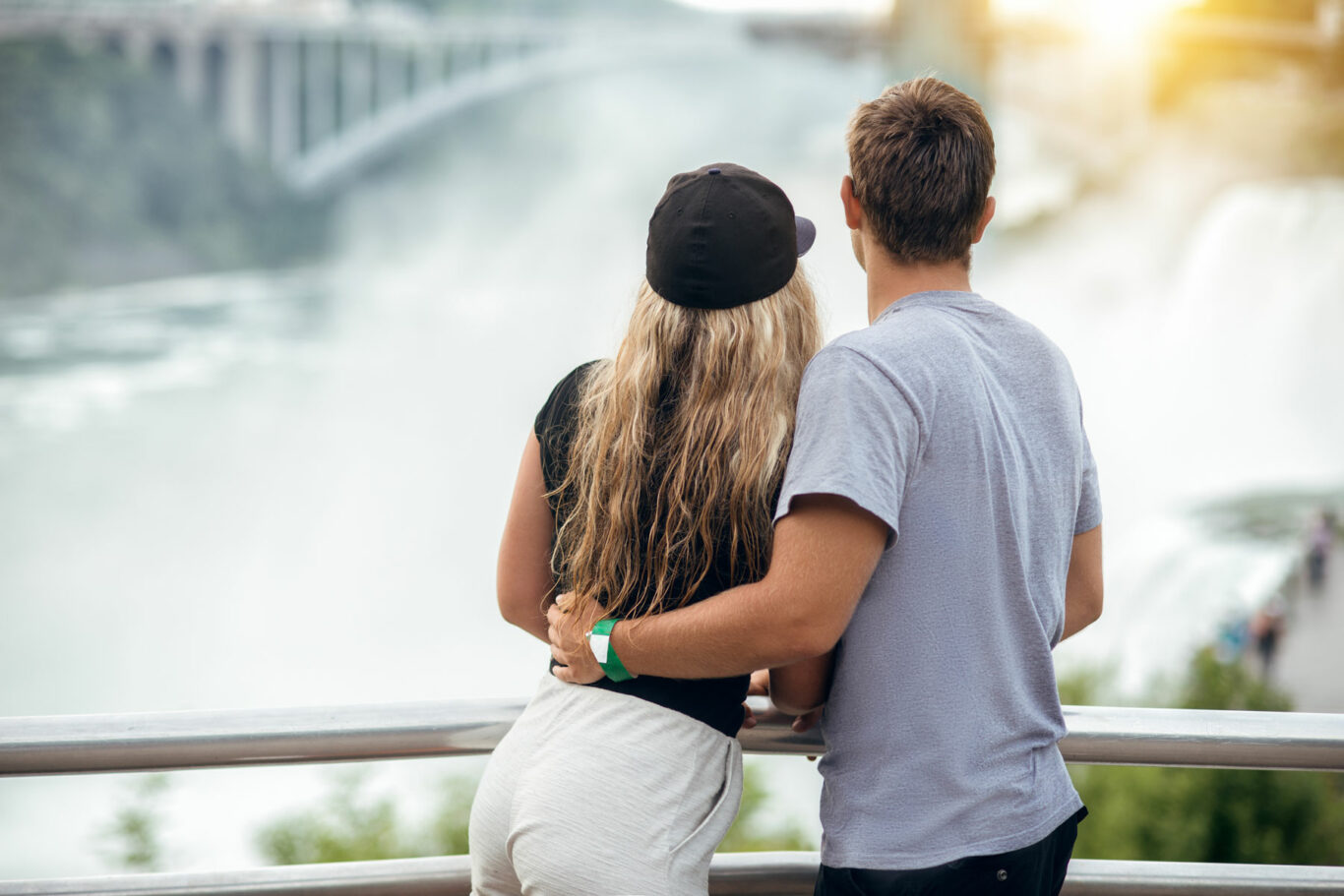 Happy tourist couple enjoying the view to Niagara Falls during romantic vacation. People looking to nature landscape at sunset time.