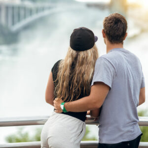 Happy tourist couple enjoying the view to Niagara Falls during romantic vacation. People looking to nature landscape at sunset time.