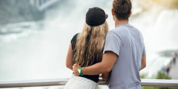 Happy tourist couple enjoying the view to Niagara Falls during romantic vacation. People looking to nature landscape at sunset time.