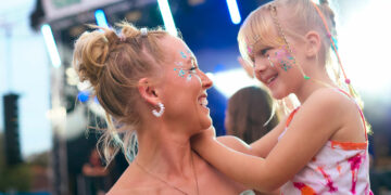 Mother With Daughter Wearing Glitter Having Fun At Outdoor Summer Music Festival