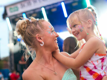 Mother With Daughter Wearing Glitter Having Fun At Outdoor Summer Music Festival