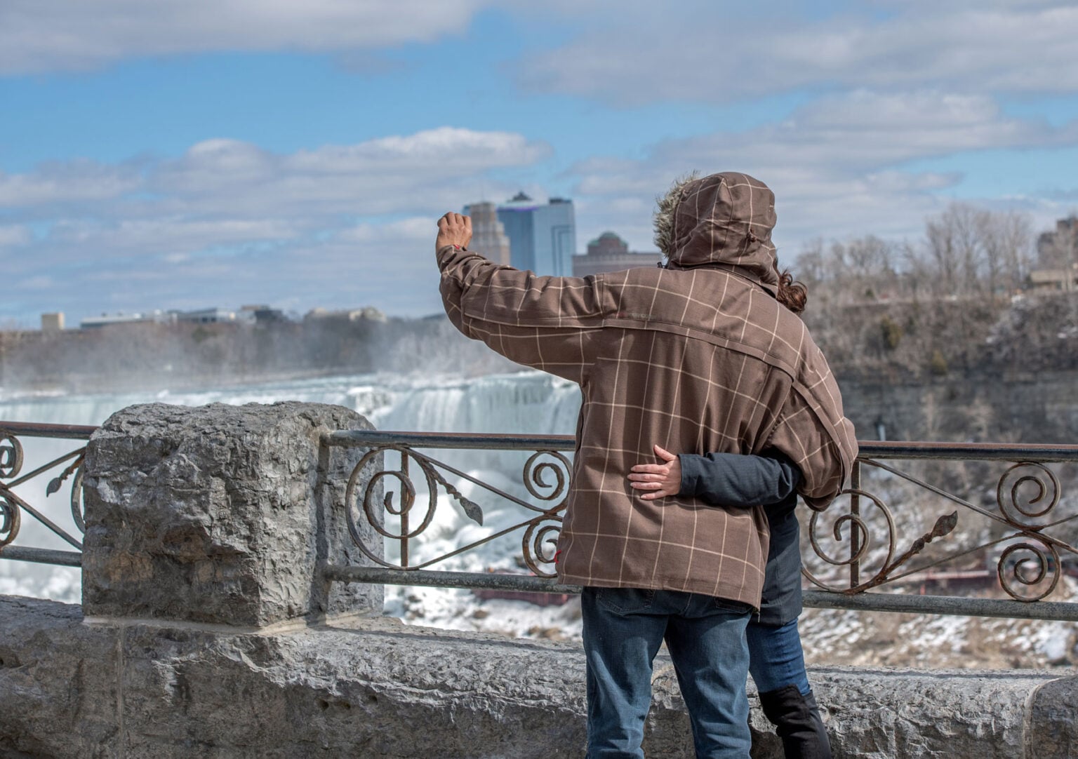 A couple embrace by Niagara Falls as they take a photograph of themselves on their mobile phone