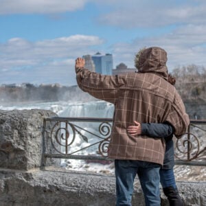 A couple embrace by Niagara Falls as they take a photograph of themselves on their mobile phone