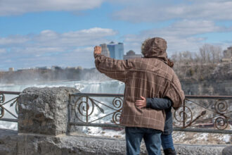 A couple embrace by Niagara Falls as they take a photograph of themselves on their mobile phone