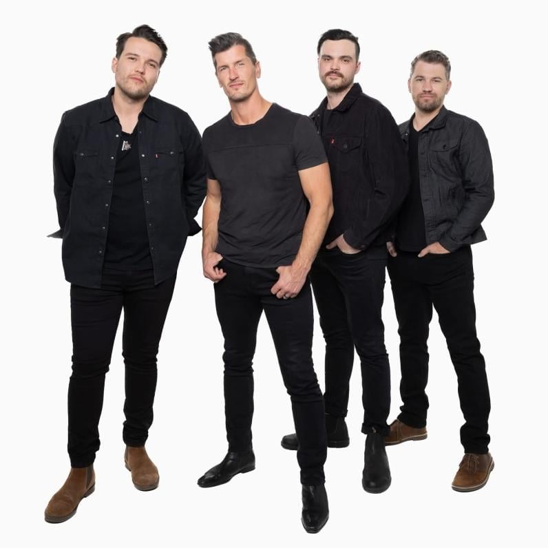 Four band members dressed in black, standing with their hands in their pockets