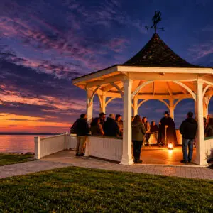 Ghost tour group gathers around a lantern-lit storyteller in a waterfront gazebo in Niagara-on-the-Lake at sunset.