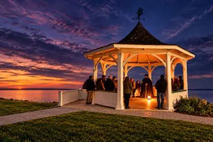 Ghost tour group gathers around a lantern-lit storyteller in a waterfront gazebo in Niagara-on-the-Lake at sunset.