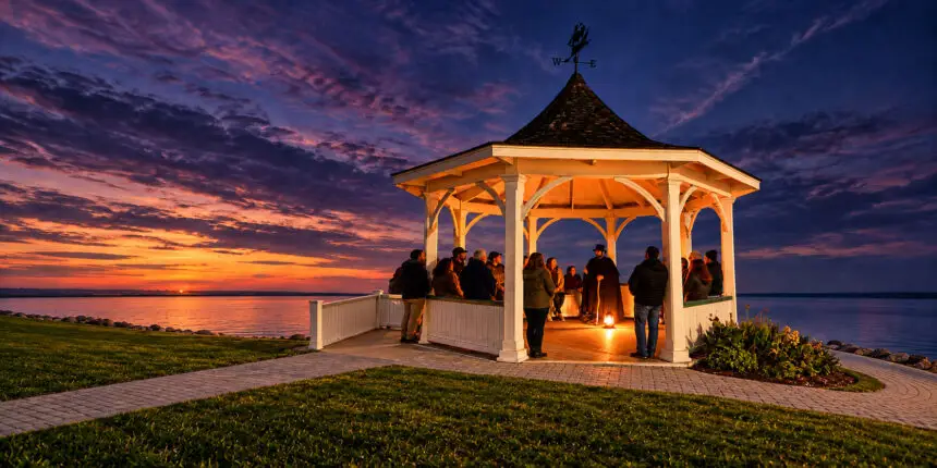 Ghost tour group gathers around a lantern-lit storyteller in a waterfront gazebo in Niagara-on-the-Lake at sunset.