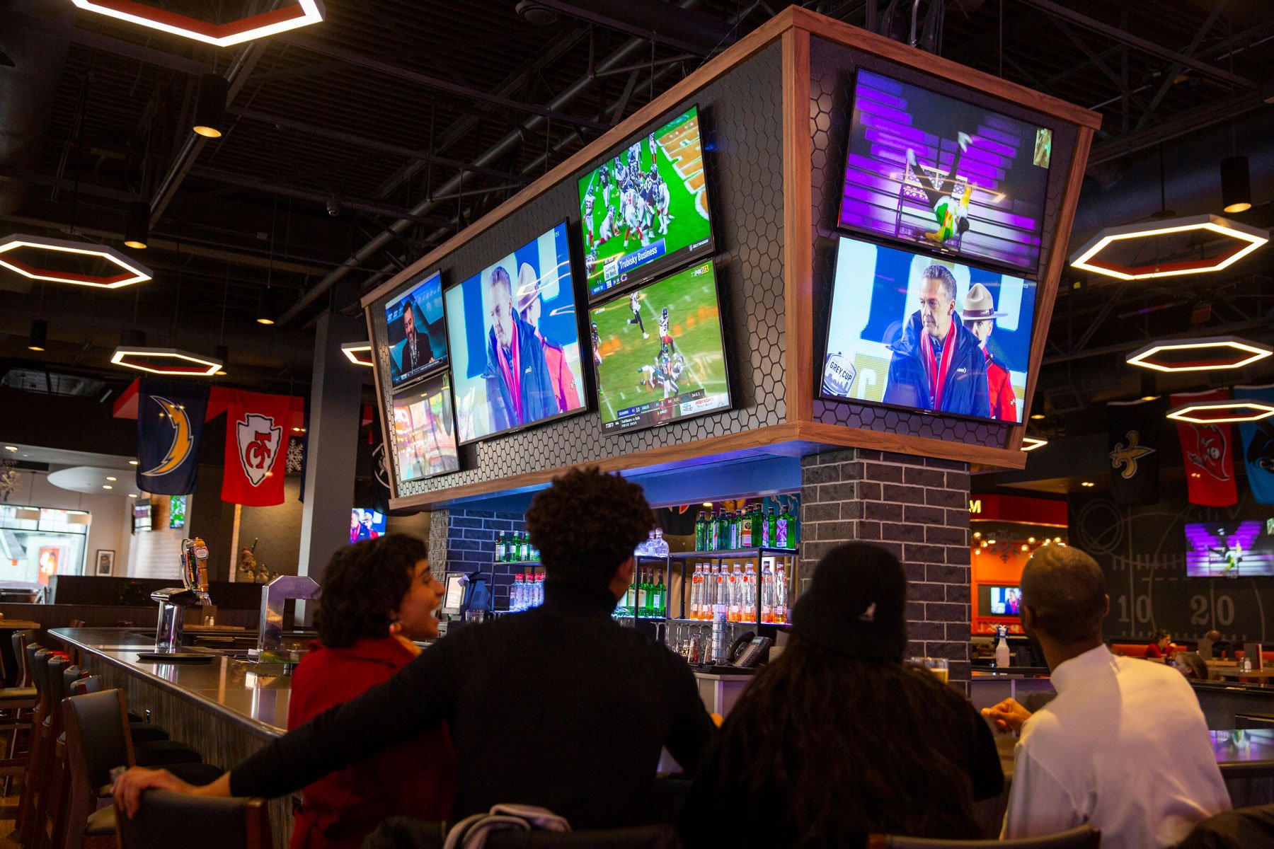 group of friends watching sports match with large screens above bar