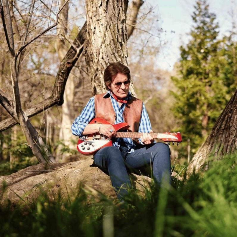 John sits on a tree trunk with a guitar in his hands