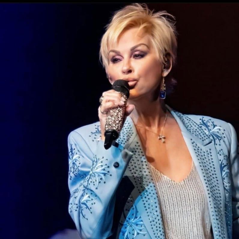 Lorrie Morgan wearing a jean jacket with short blonde hair holding a microphone