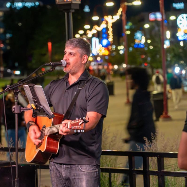 Chris Cicchino playing guitar on the patio with city lights along the strip in the background