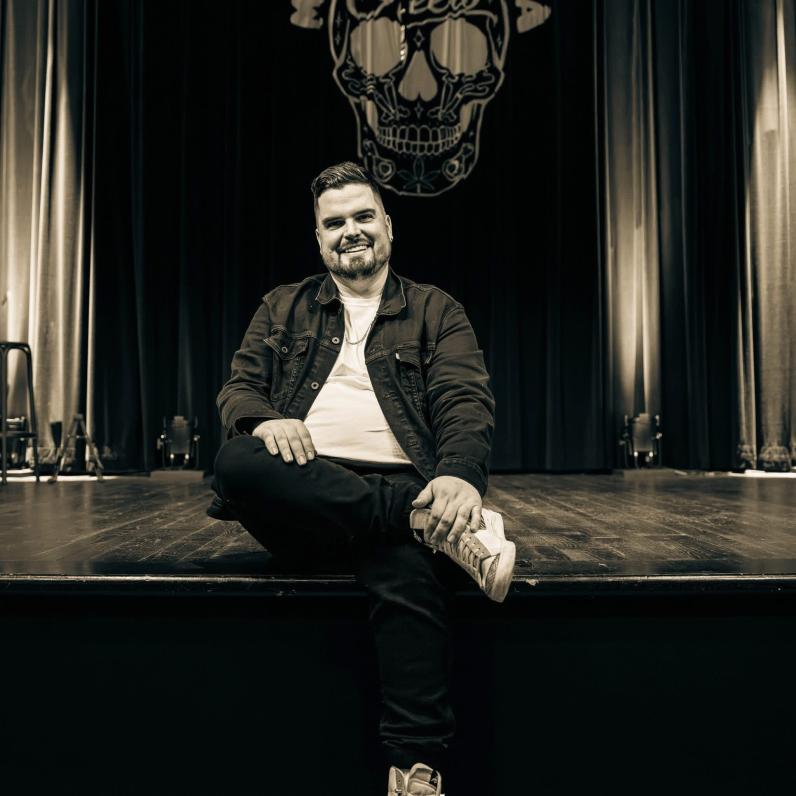 Mike Rita sitting on the edge of a stage