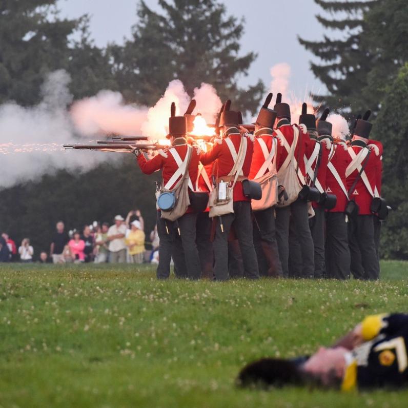 reenactors dressed as british soldiers with rifles raised and fired