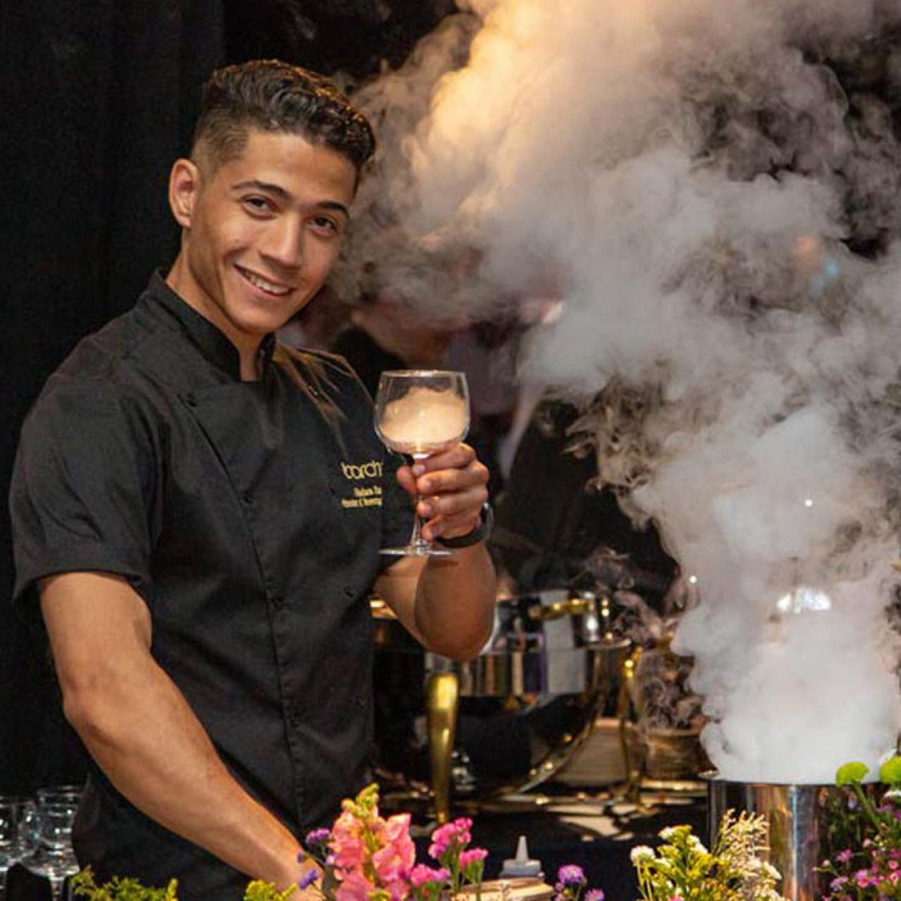 man holding a drink with a smokey background