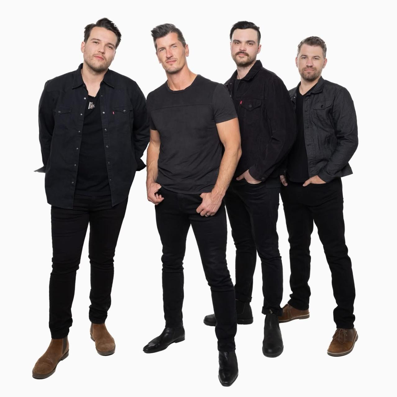 Four band members dressed in black, standing with their hands in their pockets 
