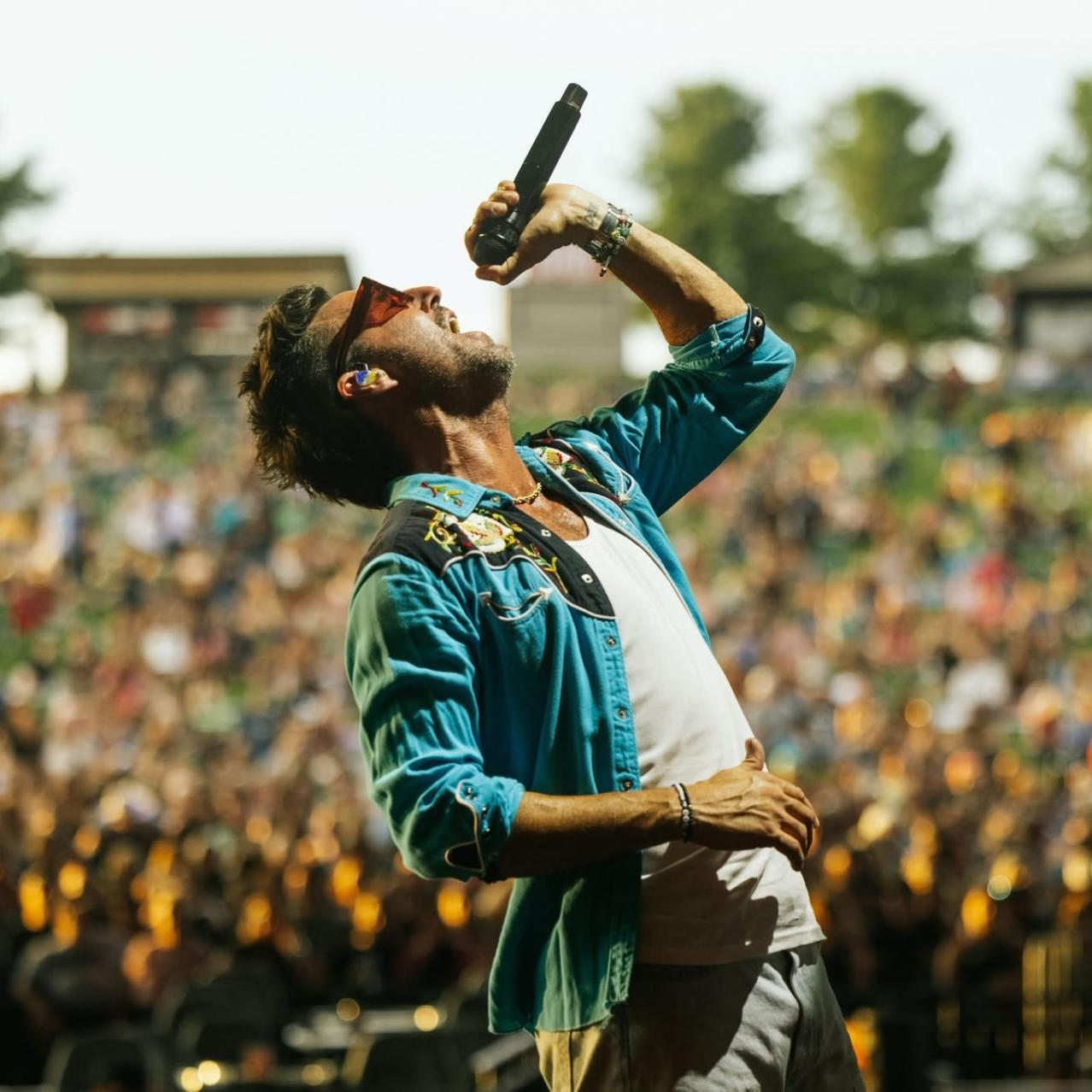 Jake Owen on stage with microphone in his hand. Fans in the audience cheering.
