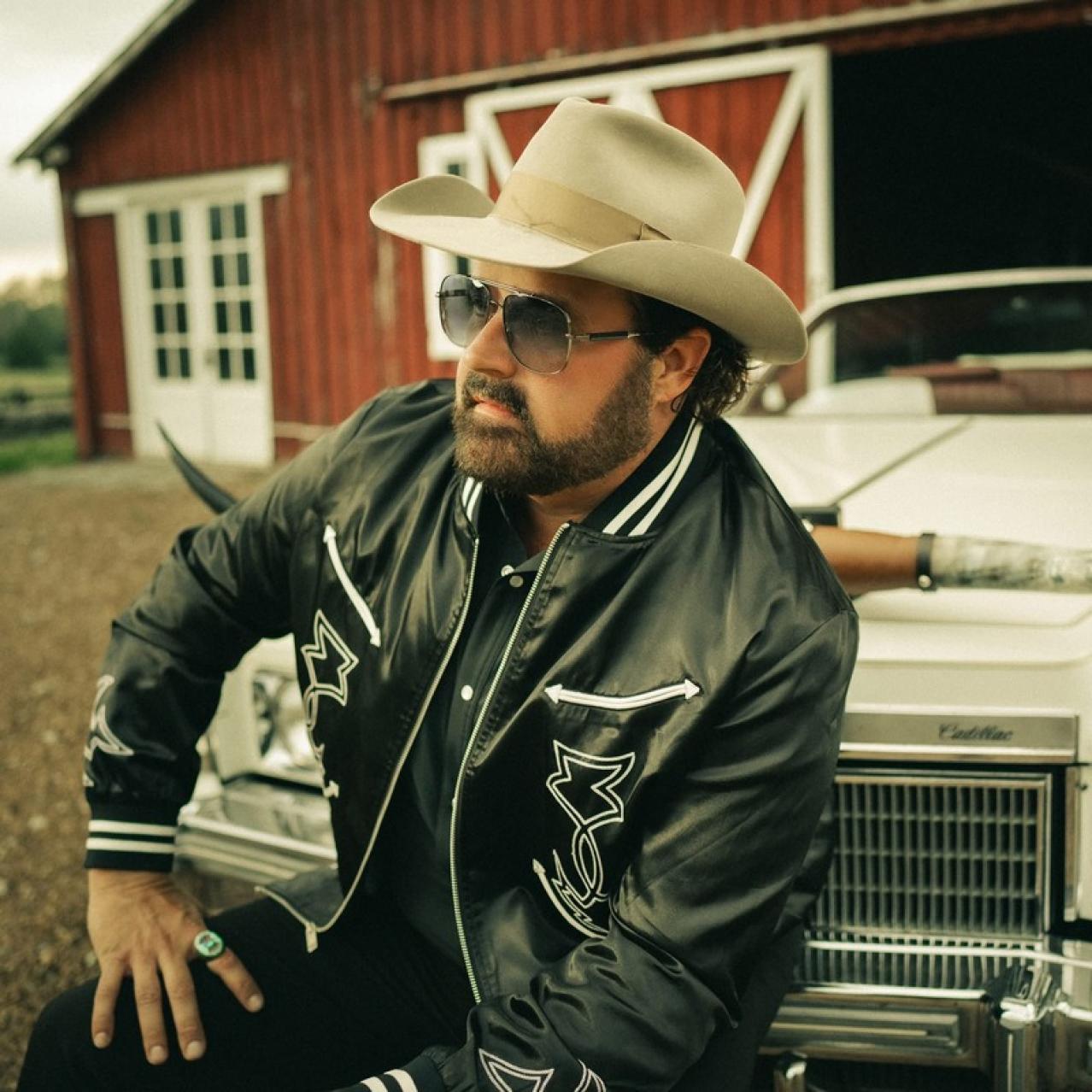 Randy sitting on the edge of his car bumper wearing a cowboy hat and glasses