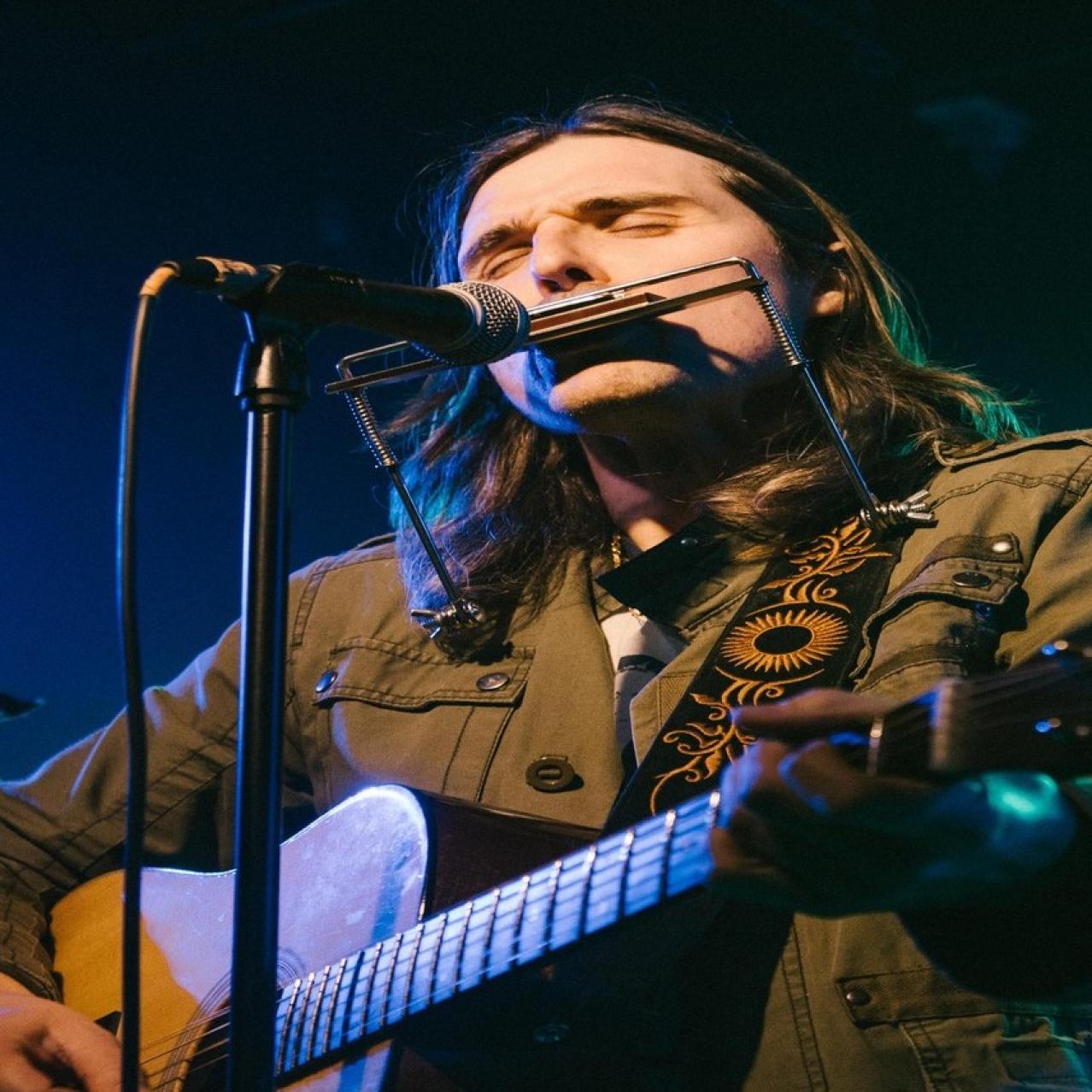 Taylor Barber on stage with a guitar and harmonica