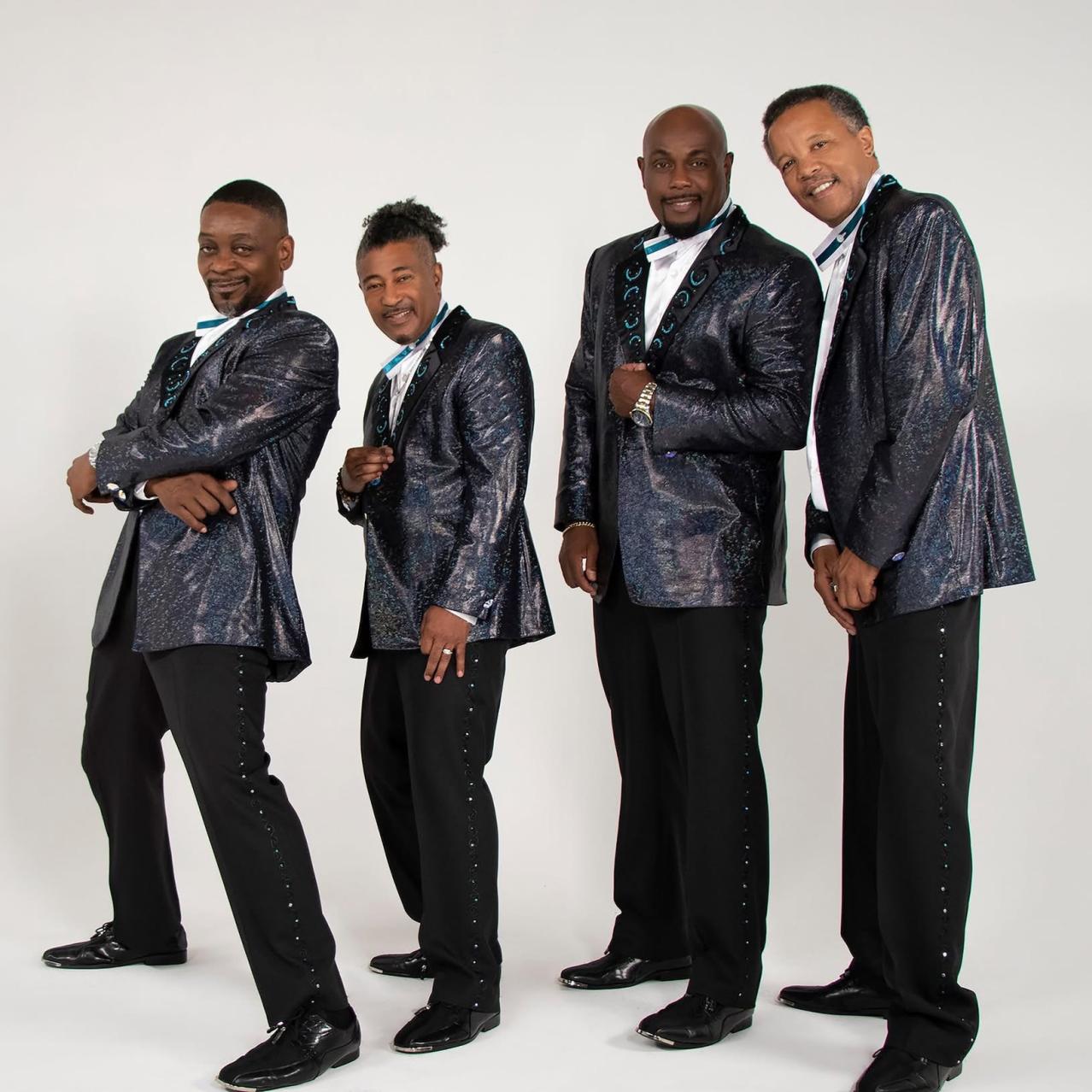 Band members standing with a white background wearing dark grey\black suits