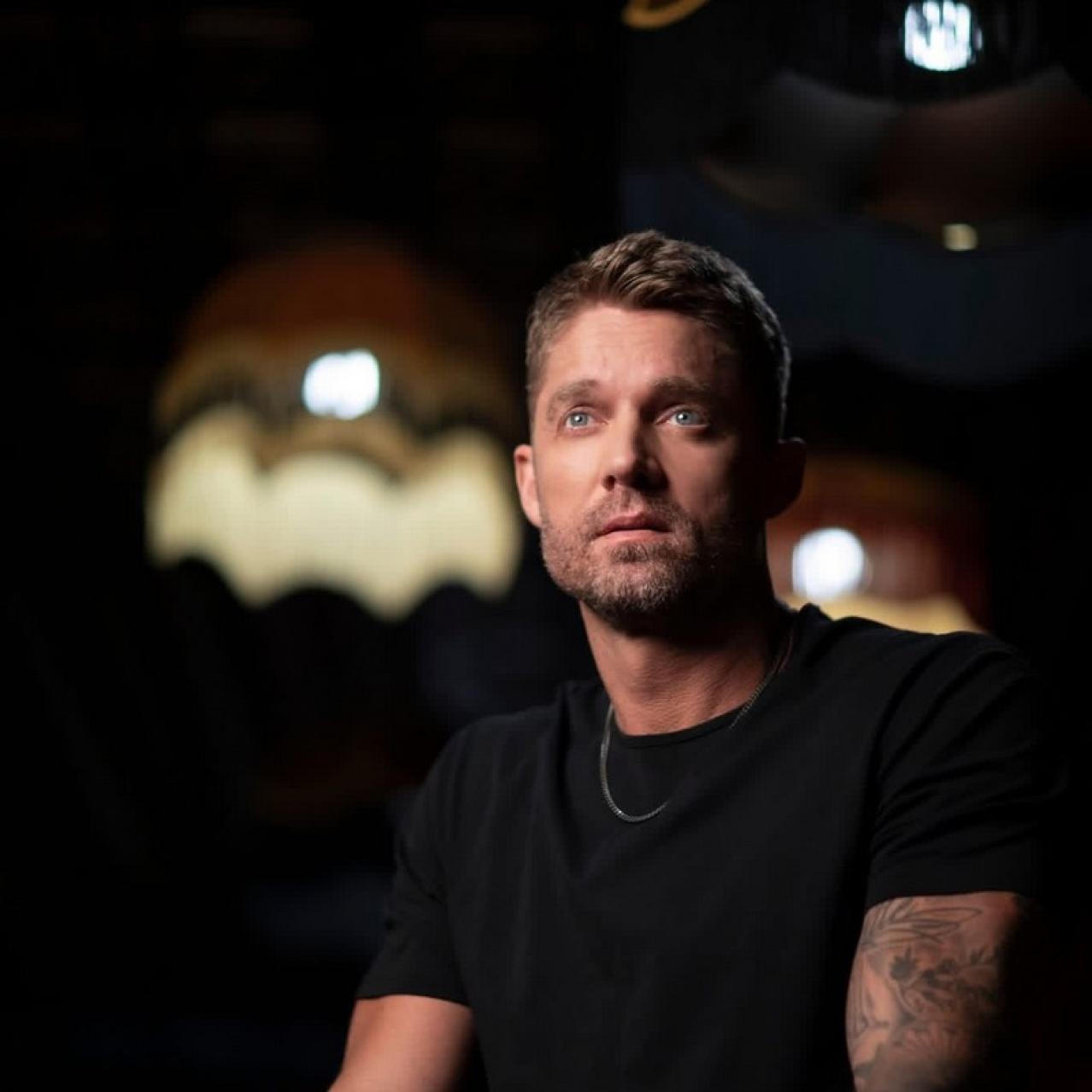 Brett Young in a black t shirt with lampshades in the background