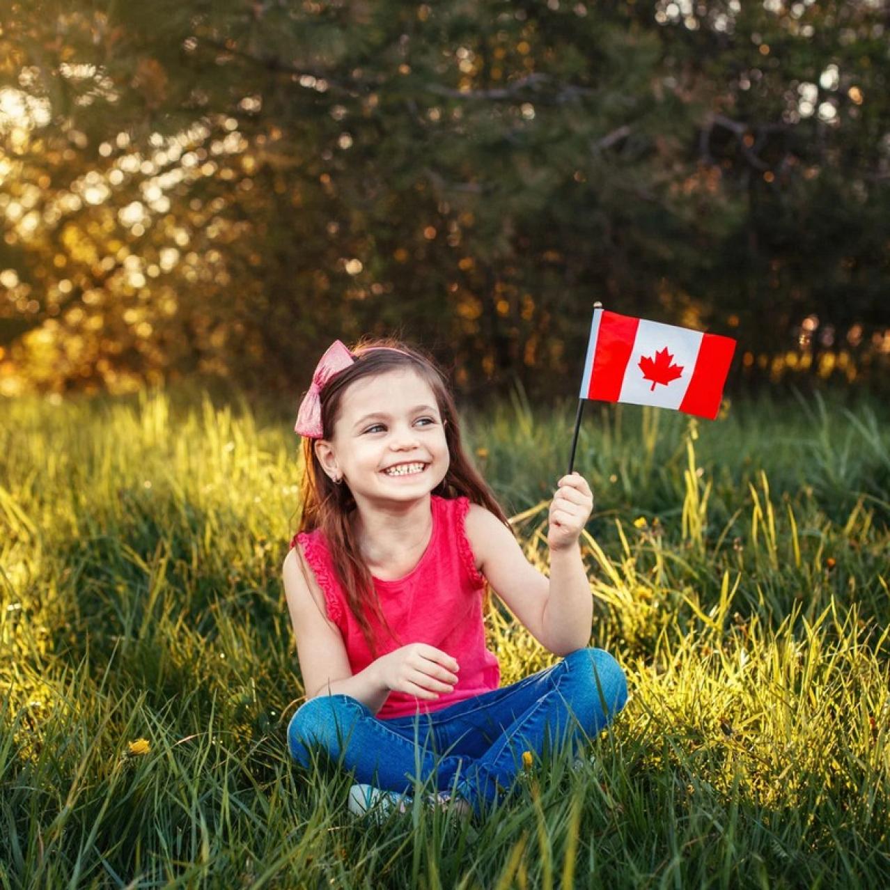Young girl sitting in the grass with a red shit on holding a small Canada flag