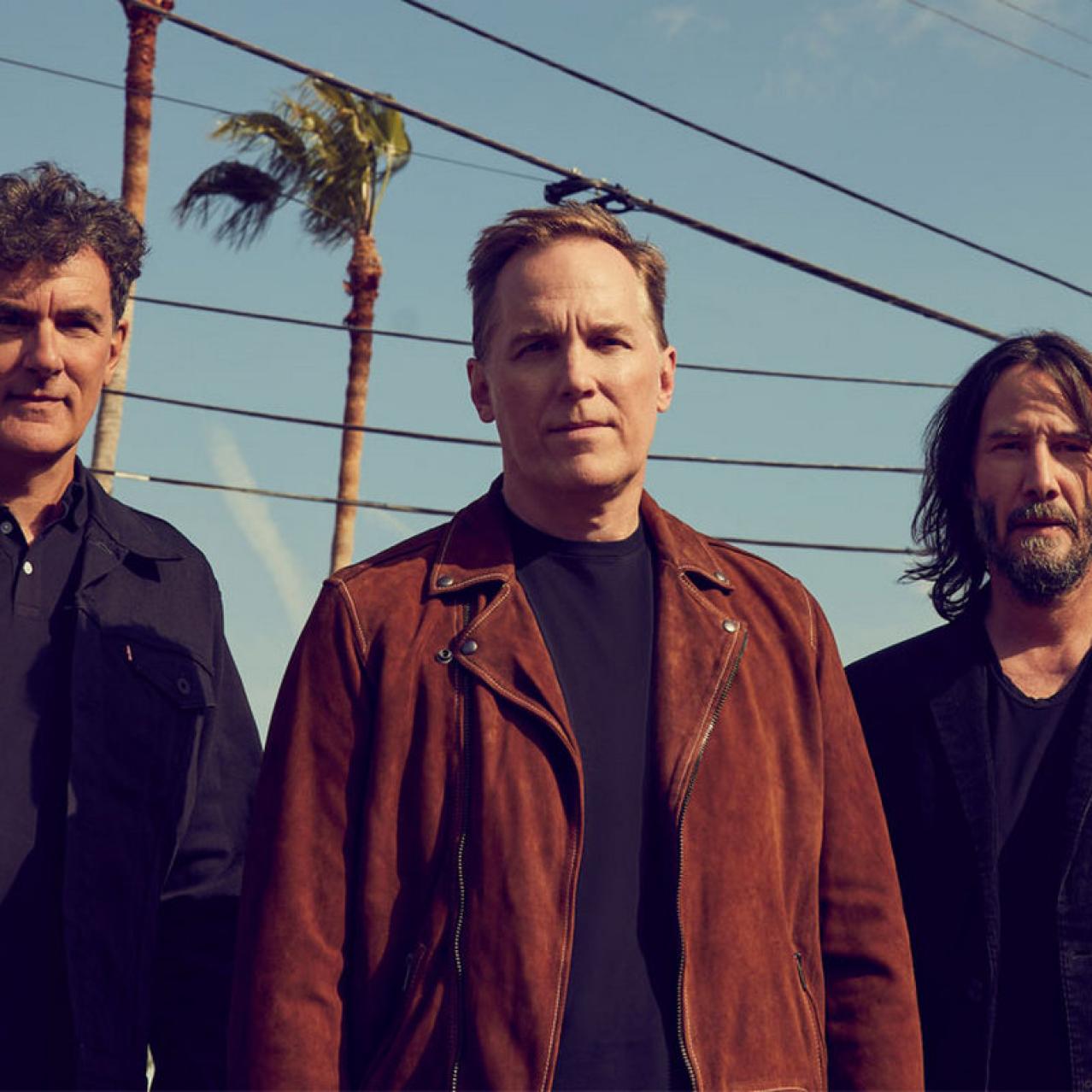 Trio standing with electric lines and palm trees in the background