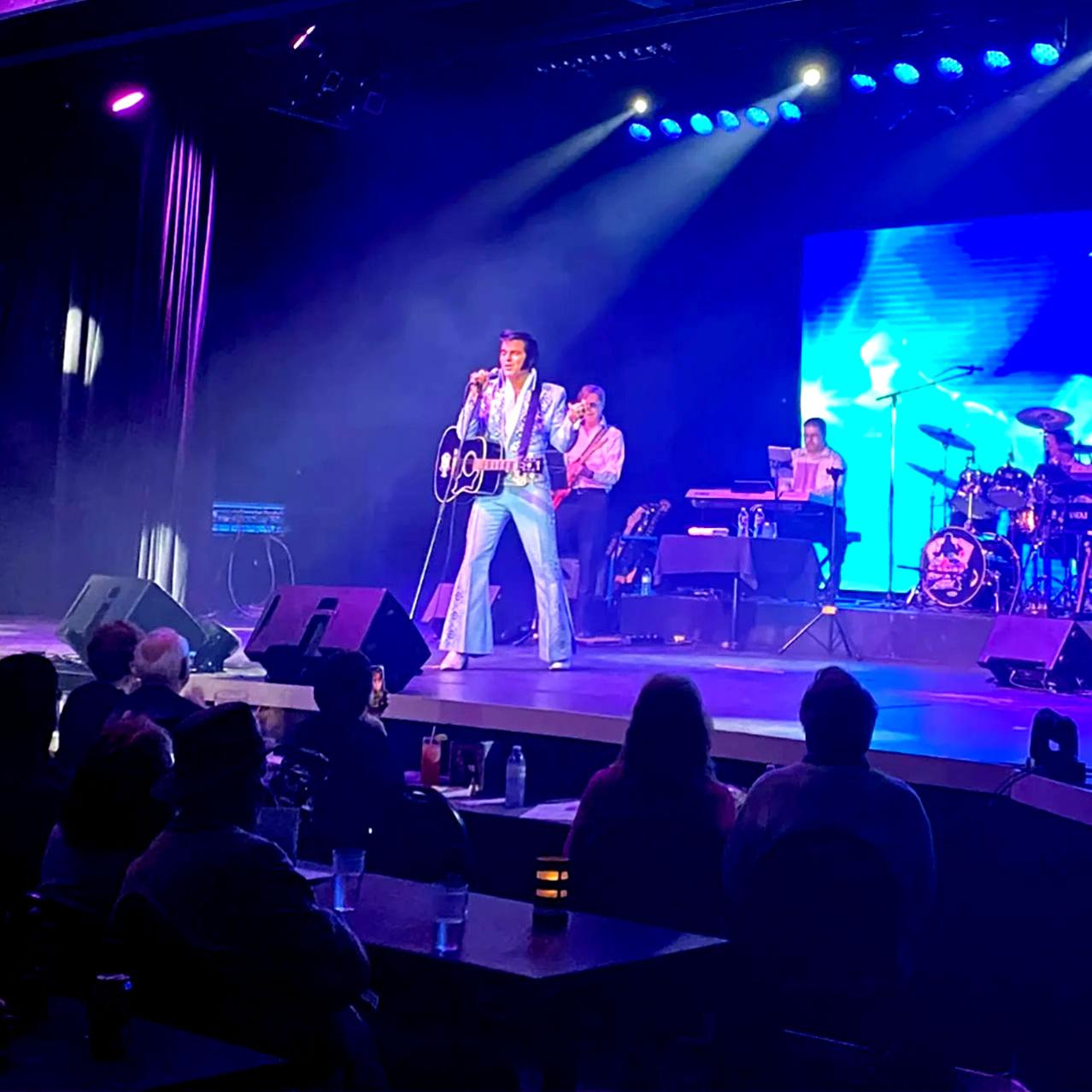 Elvis with a guitar standing in front of an audience with a red background