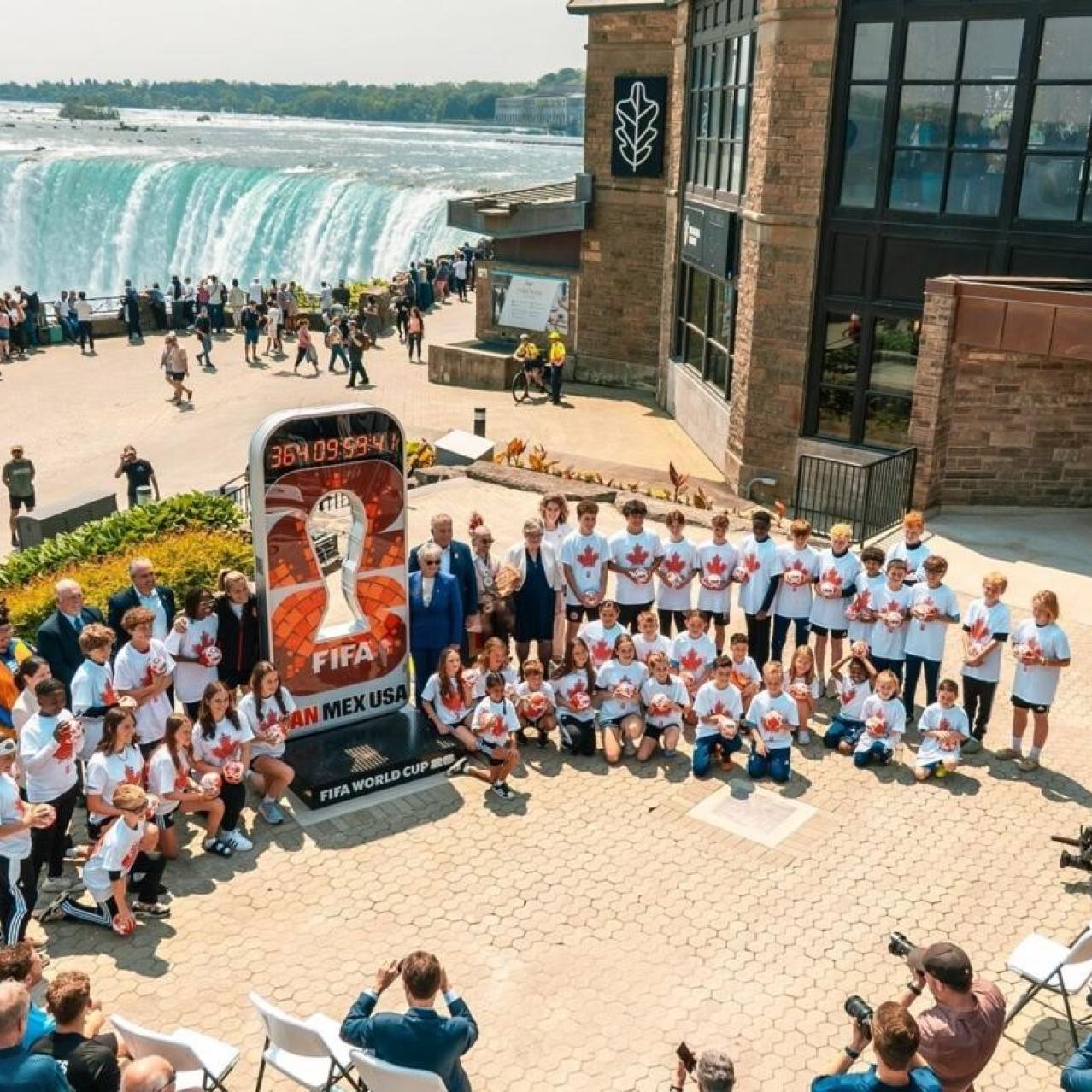 A group of people standing in front of the FIFA World Cup countdown clock with the falls in the background