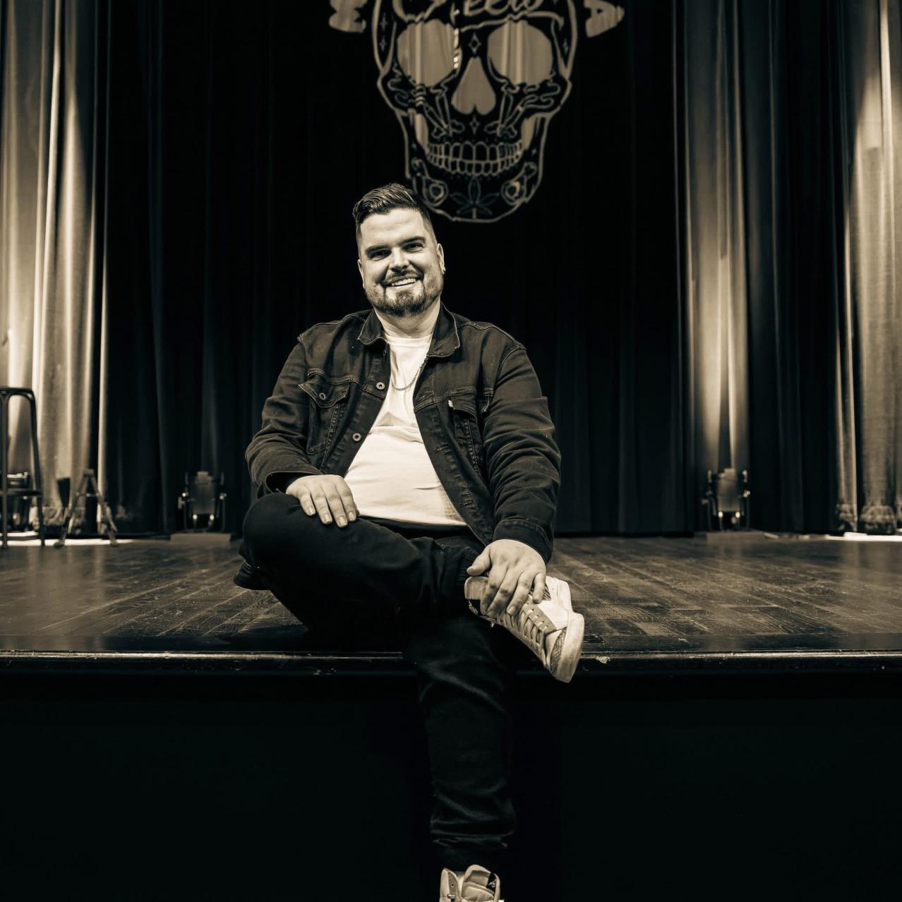 Mike Rita sitting on the edge of a stage