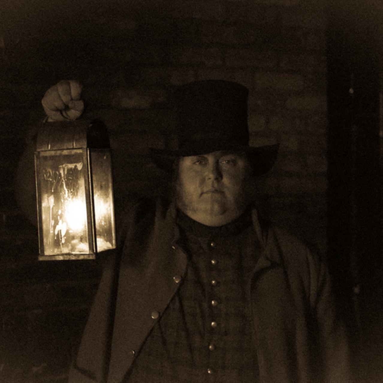 Guide holding a candlelit lamp and wearing a top hat