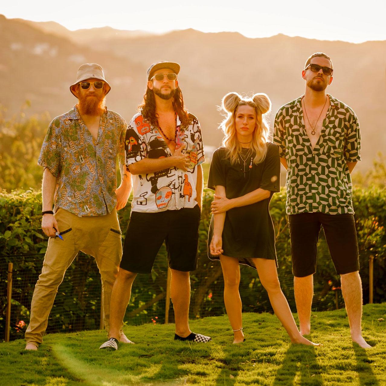 Walk off the Earth bandmembers standing on the grass with mountains in the background
