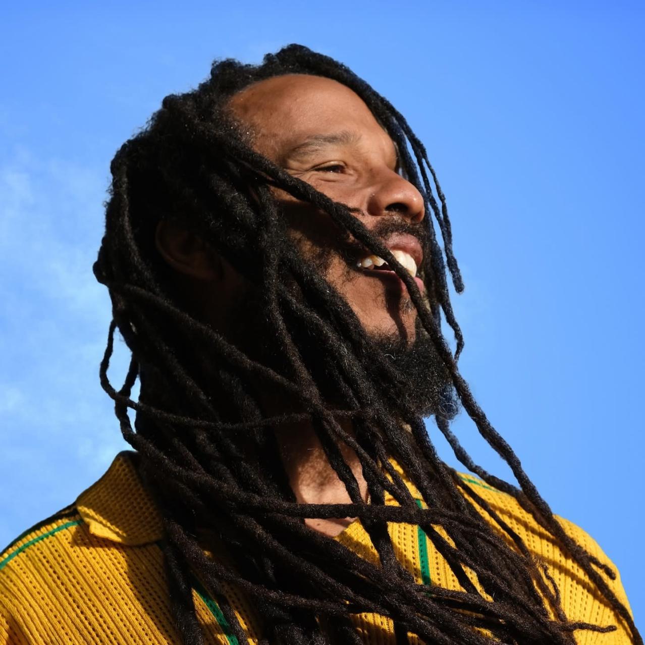 Ziggy Marley in a yellow shirt with a sky blue background